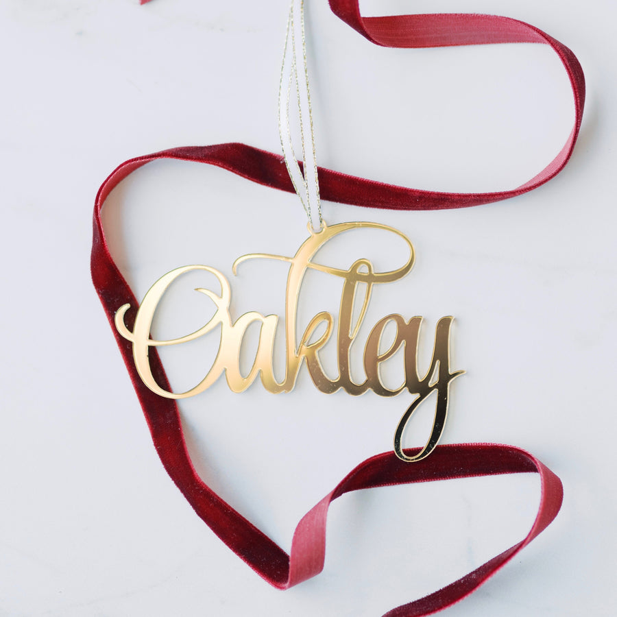 Oakley gold name Christmas ornament with red ribbon around it