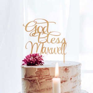 god bless Maxwell cake topper with a candle in front of white cake at a baptism