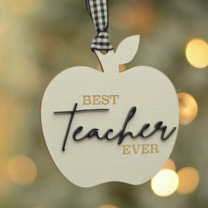 Best teacher Ever white and black ornament with twinkly lights in the background.