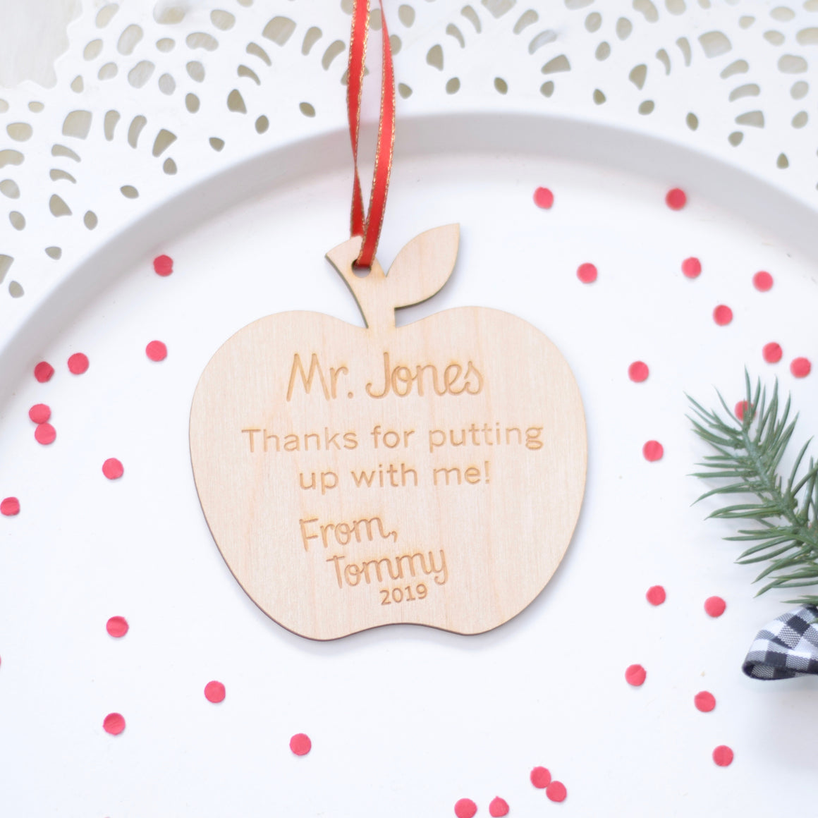 Apple Christmas tree ornament placed on a white cake plate with red confetti and Christmas greenery