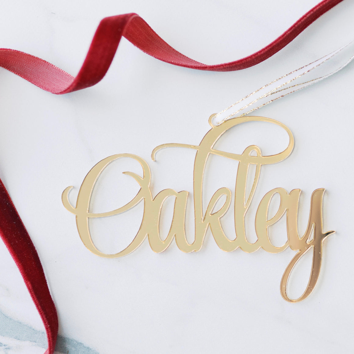 Oakley gold name Christmas ornament with red ribbon around it