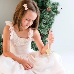 Little girl wearing pink dress holding ballerina Christmas ornament in front of green wreath