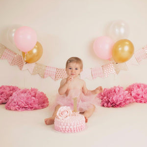 baby with a first birthday pink birthday cake, gold and pink balloons for a cake smash photo