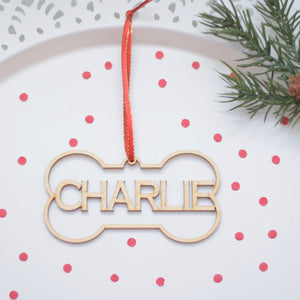 Charlie dog bone Christmas ornament on a white cake plate with red confetti and greenery
