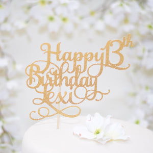 Gold happy 13th birthday cake topper on a white cake with white flowers