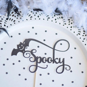 Spooky black sparkle cake topper with bat details and delicate details on a white plate background