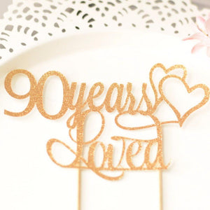 90 years loved gold sparkle cake topper with two gold intertwined hearts on white background