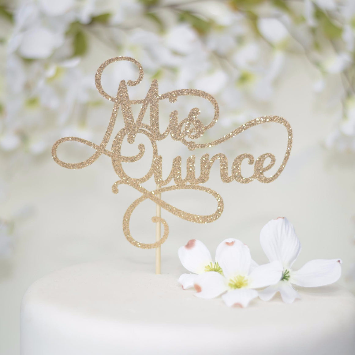 Mis Quince gold sparkle cake topper on white cake with white flowers