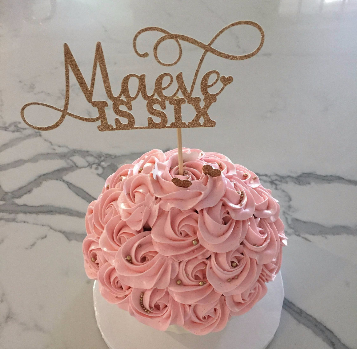 Maeve is six dark gold glitter cake topper on pink swirl cake