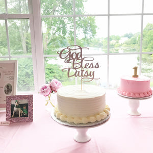 God Bless Daisy gold cake topper on beautiful ivory cake in front of a large window with natural lighting
