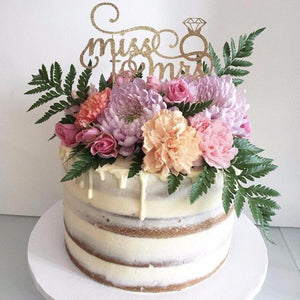 miss to mrs gold glitter cake topper with diamond ring details on a white cake with floral details
