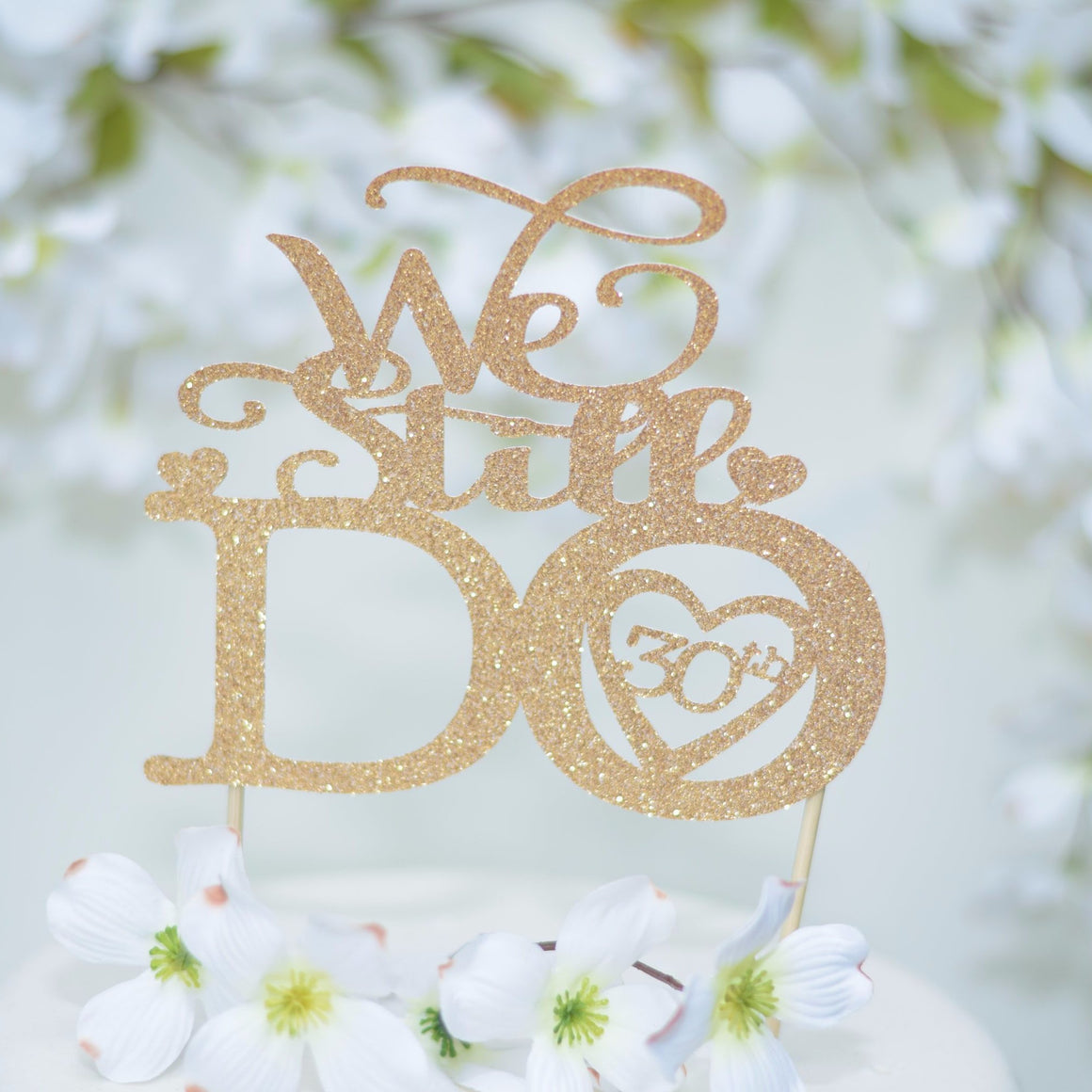 We Still Do 30th Anniversary Cake Topper in Gold Glitter font on a white wedding cake with floral background