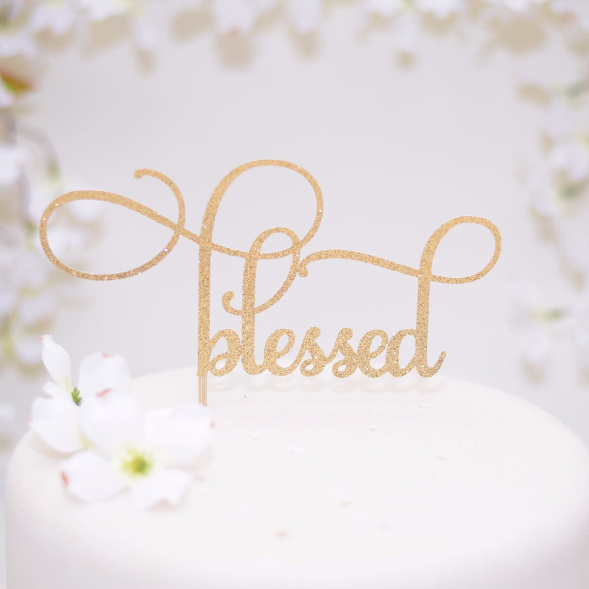 Elegant Blessed gold glitter cake topper on a white cake with floral details