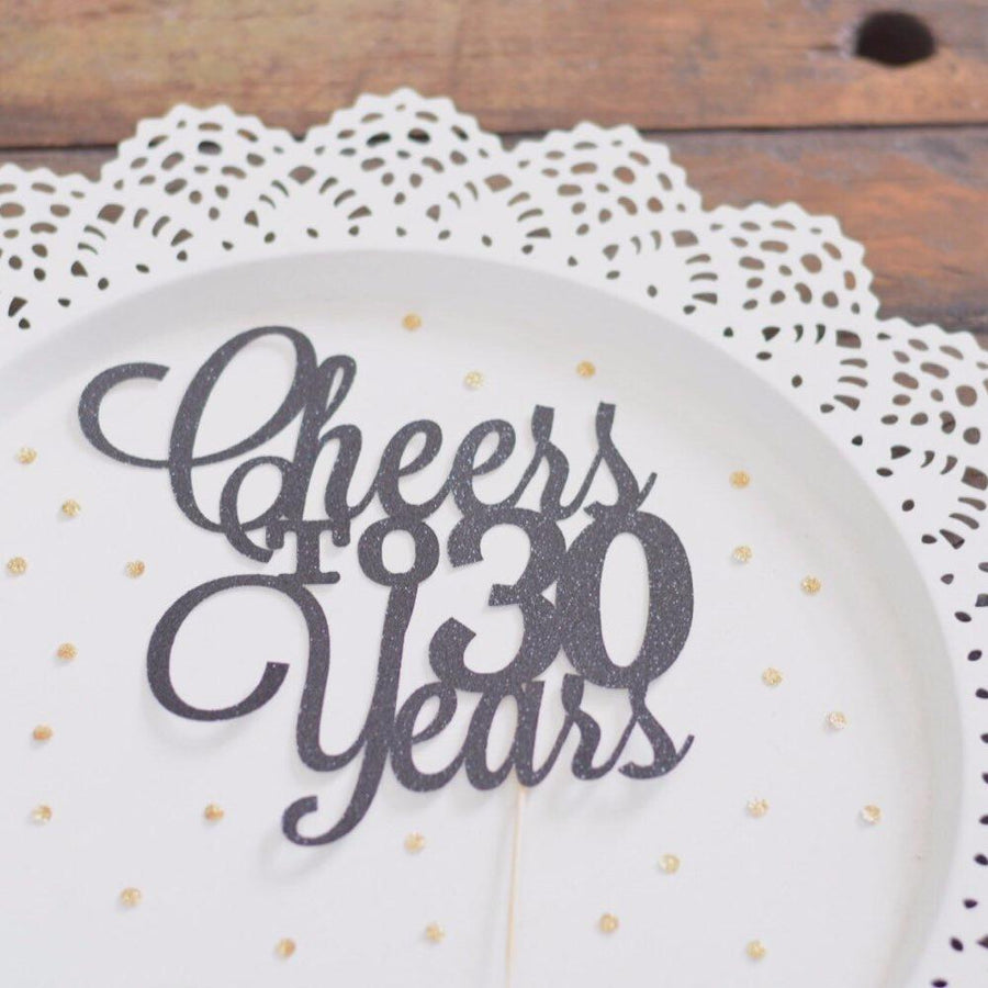 Cheers to 50 years black glitter cake topper on white plate background with black feathers