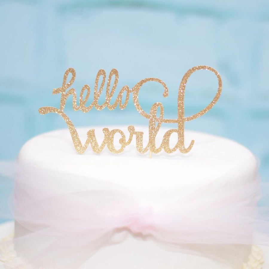 gold hello world cake topper on a silver mint and gold drip cake with daisies