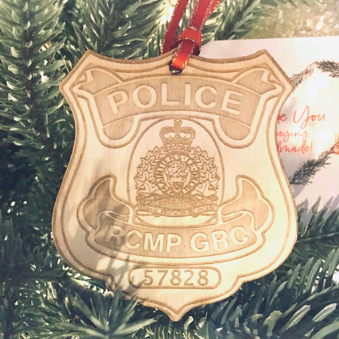 RCMP badge laser cut onto wood with a red and gold ribbon hanging on a tree