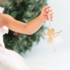 Little hand holding up a gold and white ballerina Christmas ornament