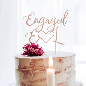 rose gold engaged cake topper on a white cake with candles and flowers